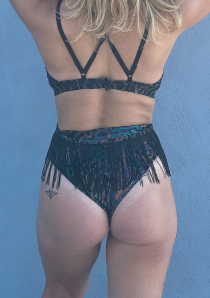 Radioactive - iridescent black leopard print -  Unisex-Festival-outfit-rave-outfit - handmade-in-Brooklyn-New York City-custom made-waste conscious- high-cut bikini bottoms – retro style – hippie fashion – rave bottoms – festival bottoms - back view on model